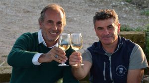 Due uomini brindano con bicchieri di vino in un ambiente all'aperto.